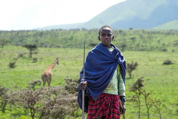       Young person in traditional attire with giraffe in background.
  