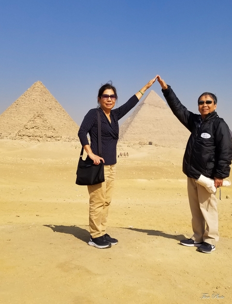 Two people posing with pyramids in the background, blue skies.