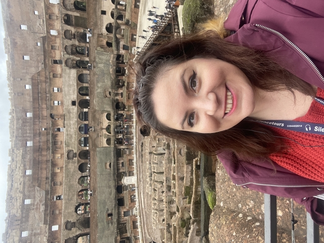      Person smiling in front of the Roman Colosseum.
  