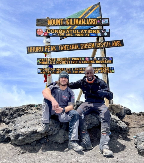 Two people smiling at Uhuru Peak with a sign in the background.