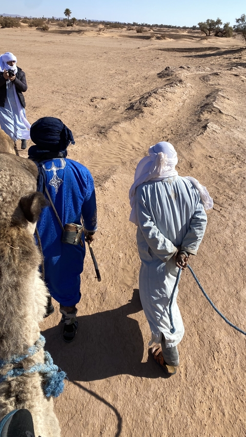 Two people walking with a camel in the desert.