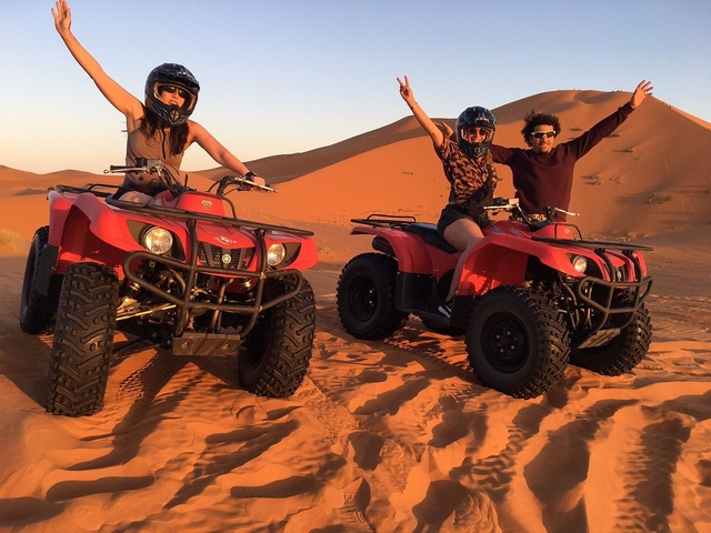       Three people on red quad bikes in a desert setting.
  
