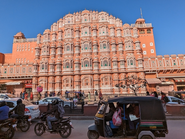       Street view of Hawa Mahal, a historical architecture with traffic and people.
  