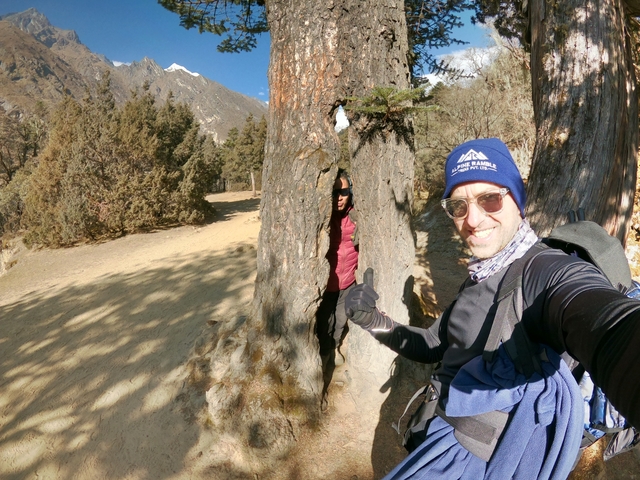 Two people outdoors, one peeking from a tree.