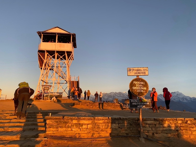 Tourists at Poon Hill viewpoint with mountains in the distance.