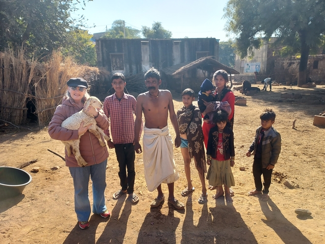       Group of people, including a person holding a small animal, in a rural setting.
  