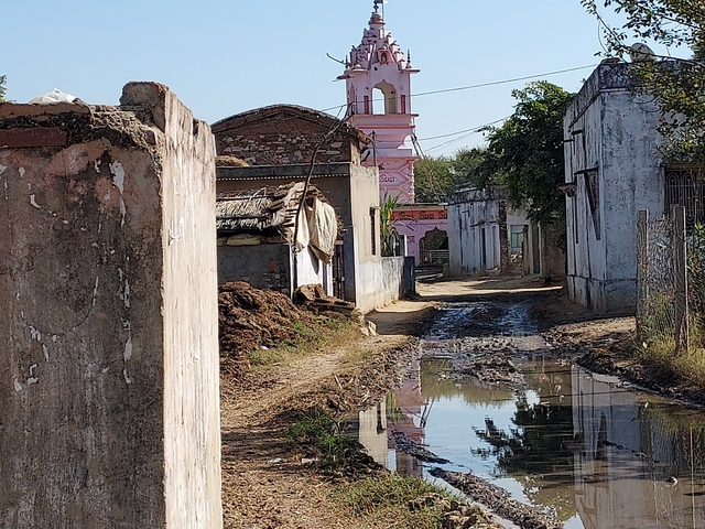       Narrow street in a village with a pink building in the background.
  