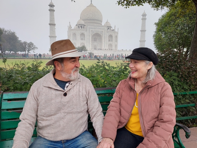       Two people sitting on a bench with the Taj Mahal in the background.
  