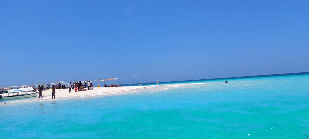 Beach with white sand and turquoise water, people in distance.