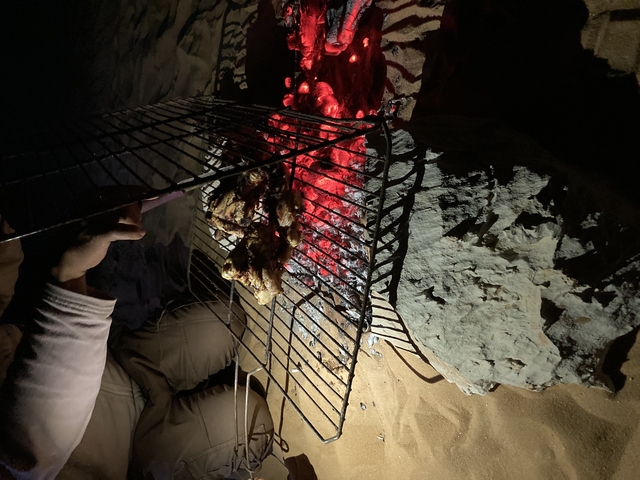 Grilling meat over a charcoal fire at night.