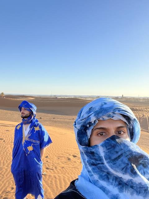 Two people in traditional attire standing on sand dunes.
