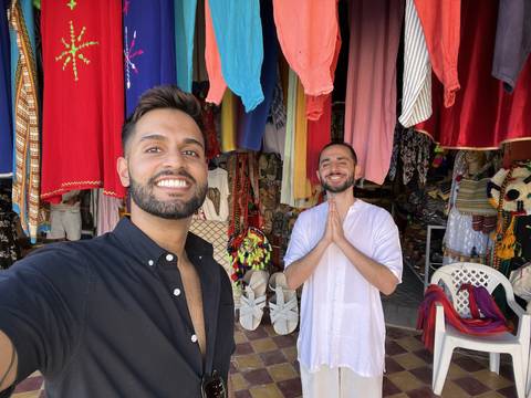 Two people smiling at a vibrant market with clothing.