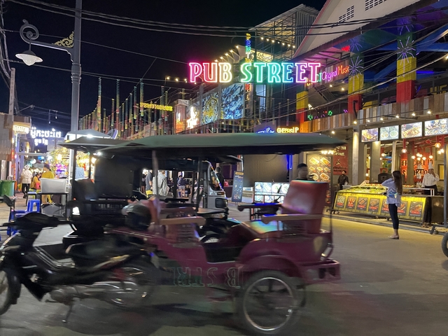       Busy street scene with neon signs and tuk-tuks.
  