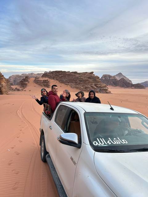 People leaning out of a white vehicle in the desert.