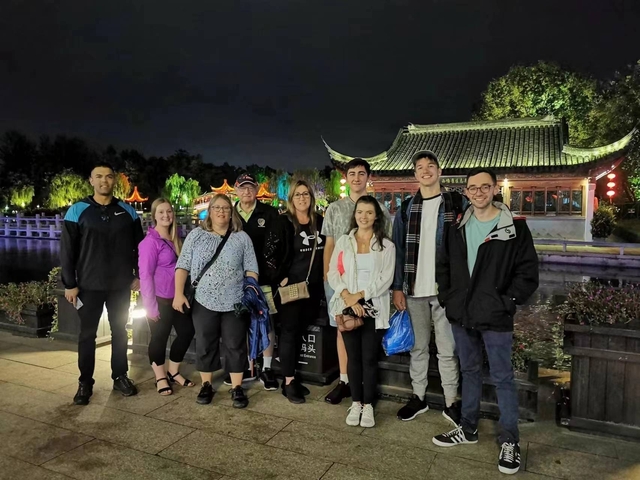       Group posing in front of a lit-up pavilion at night.
  