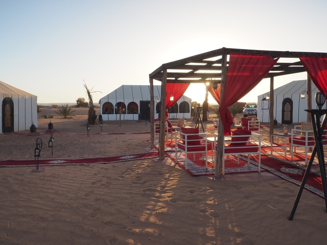 Desert campsite with tents and seating area under red drapes.