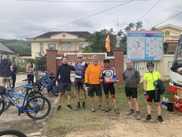       Cyclists posing outdoors with bicycles.
  