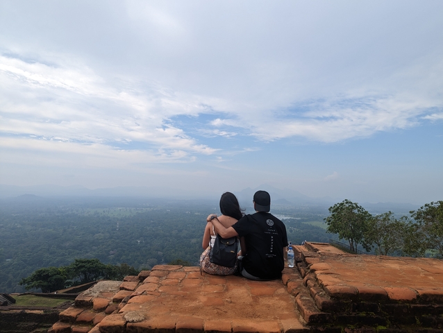       Couple sitting on a viewpoint with a vast landscape ahead.
  