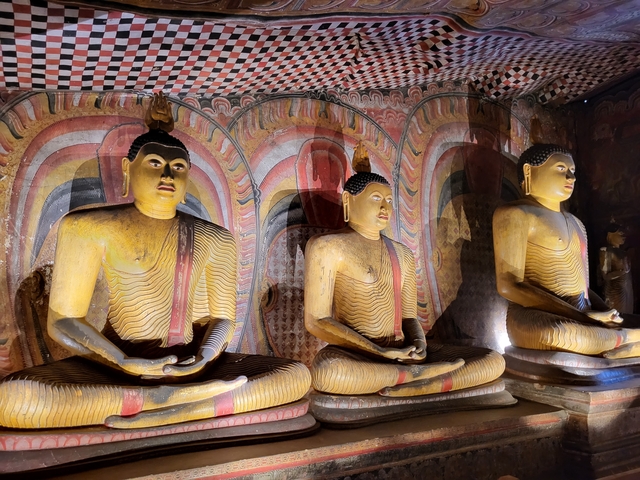       Three ancient statues of Buddha in a cave with ornate wall art.
  