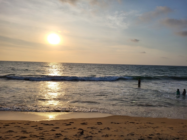       People enjoying a sunset on the beach with waves crashing.
  
