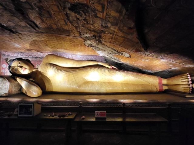      A reclining buddha statue inside a cave with ornate ceilings.
  