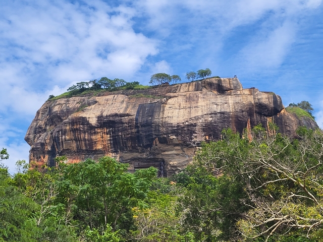       The Sigiriya Rock with trees below under a clear blue sky.
  