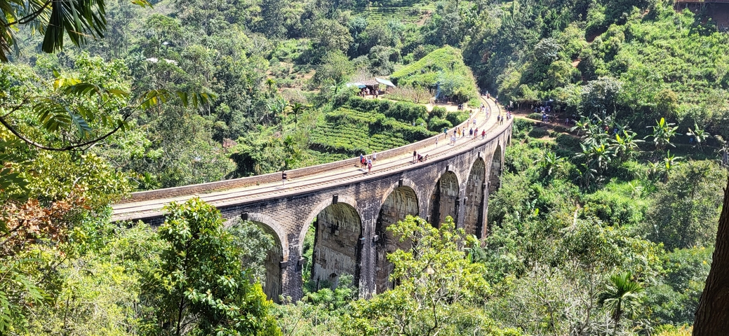       Nine Arch Bridge with people walking on it and lush greenery.
  
