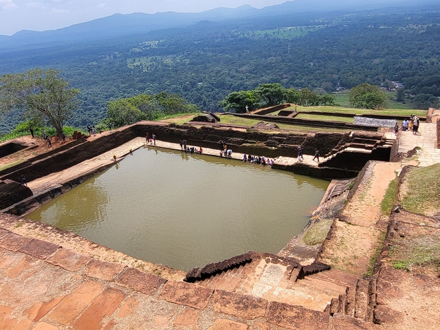       A terrace view with ancient ruins and a large pool.
  