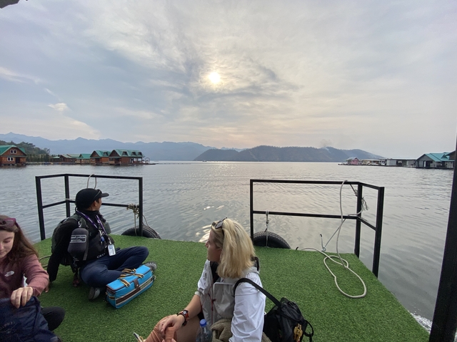       People seated on a floating deck with houseboats in the background.
  