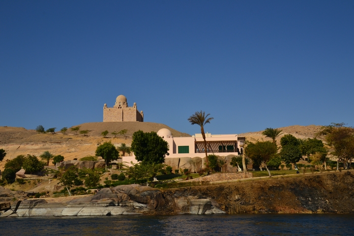 A pink stone building set on a hillside with palm trees and desert surroundings.