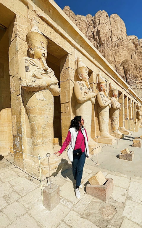       Person standing in front of large ancient statues.
  