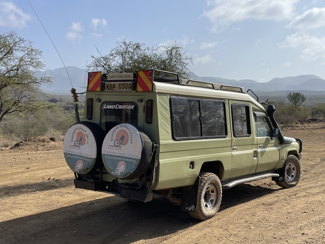 Safari vehicle on a dirt road with mountains in the background.