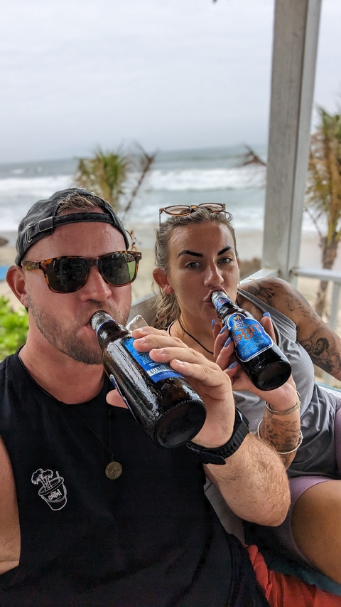 A couple enjoying bottled drinks, with a scenic background.