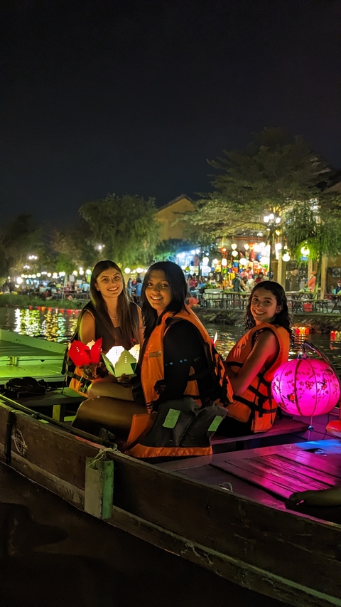       Three people wearing life vests, holding candles on a boat lit by lanterns.
  