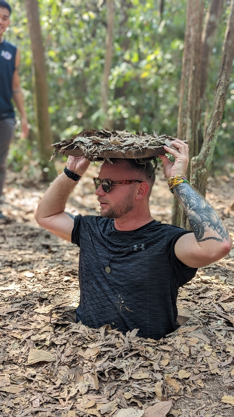       Man holding a large leaf for shade in a forest setting.
  