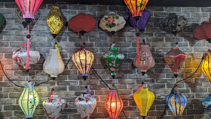       Various colorful lanterns hanging against a brick wall.
  