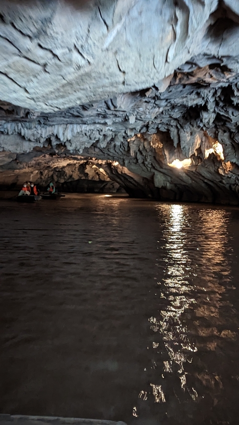 People in a boat inside a cave with water reflecting light.