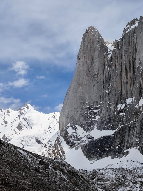 Massive rocky cliff face with snow-covered peaks in the background.