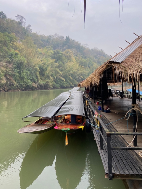       Wooden longboats docked by a riverbank with a hut.
  