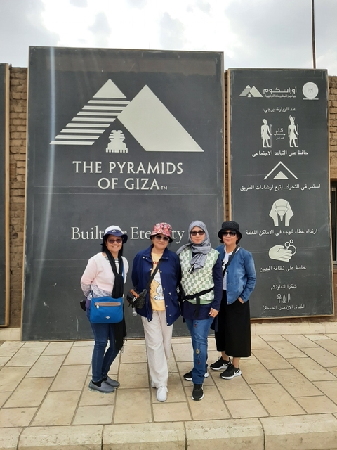 Four people posing next to a sign about the Pyramids of Giza.