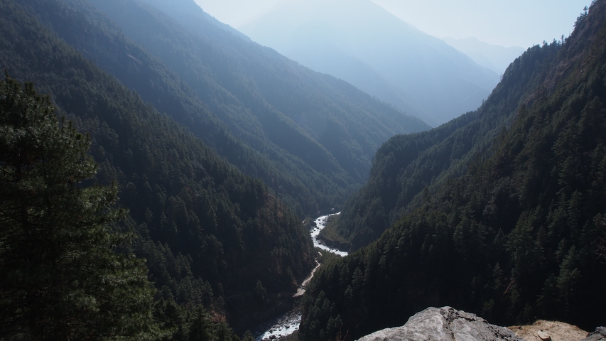       A deep valley with dense green forests and a river running through it.
  