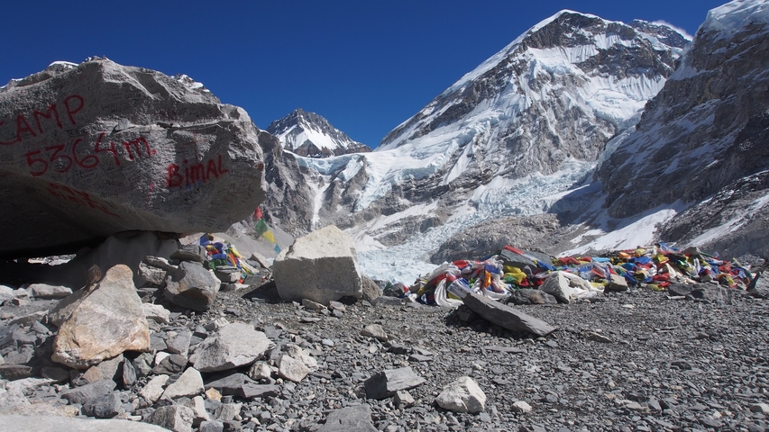       Everest Base Camp surrounded by high snowy peaks and colorful prayer flags.
  
