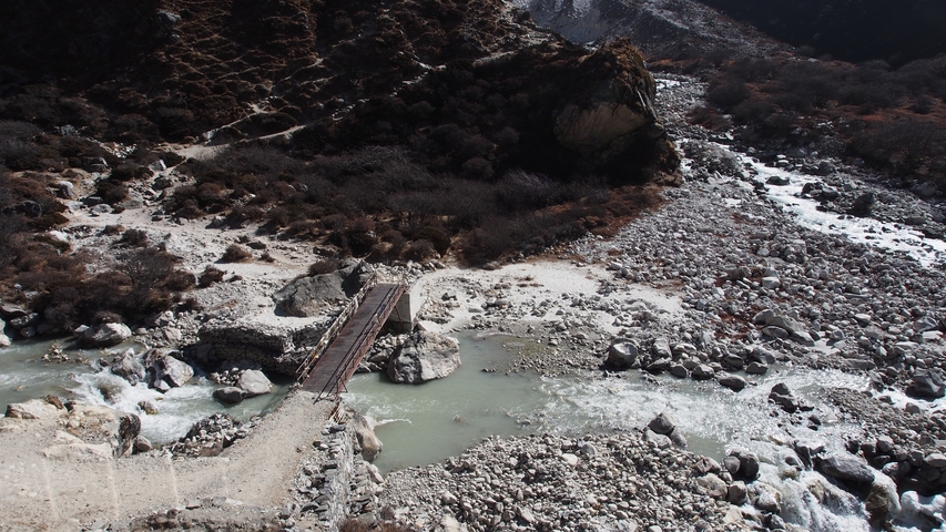       A narrow bridge over a river in a rocky landscape.
  