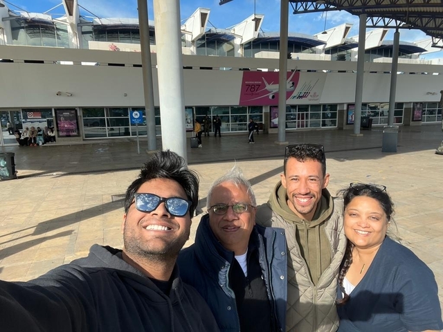       Group of people smiling in front of an airport.
  