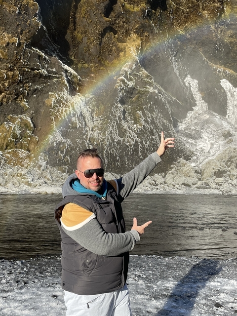       Person pointing at a rock formation with slight rainbow visible.
  
