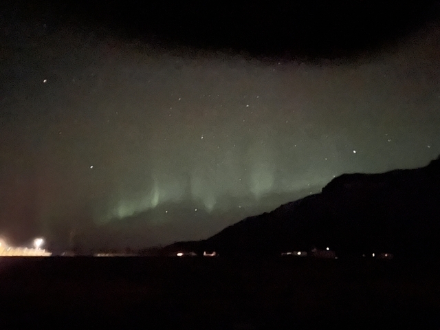       Night sky with faint Northern Lights visible over a mountaintop.
  