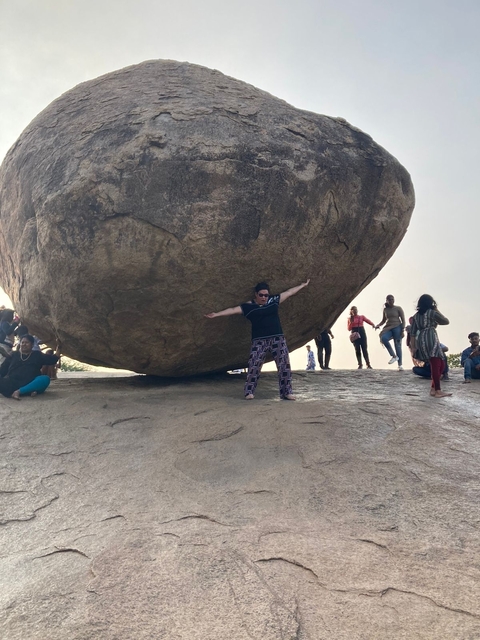       A person posing happily under a large balancing rock.
  