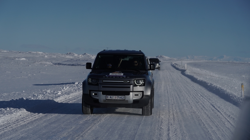 A car driving on a snowy road surrounded by mountains.
