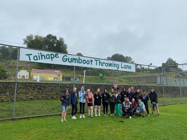A group posing beneath a sign for a gumboot throwing lane.