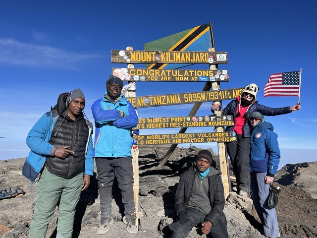 Group posing at the summit with a sign for Mount Kilimanjaro.